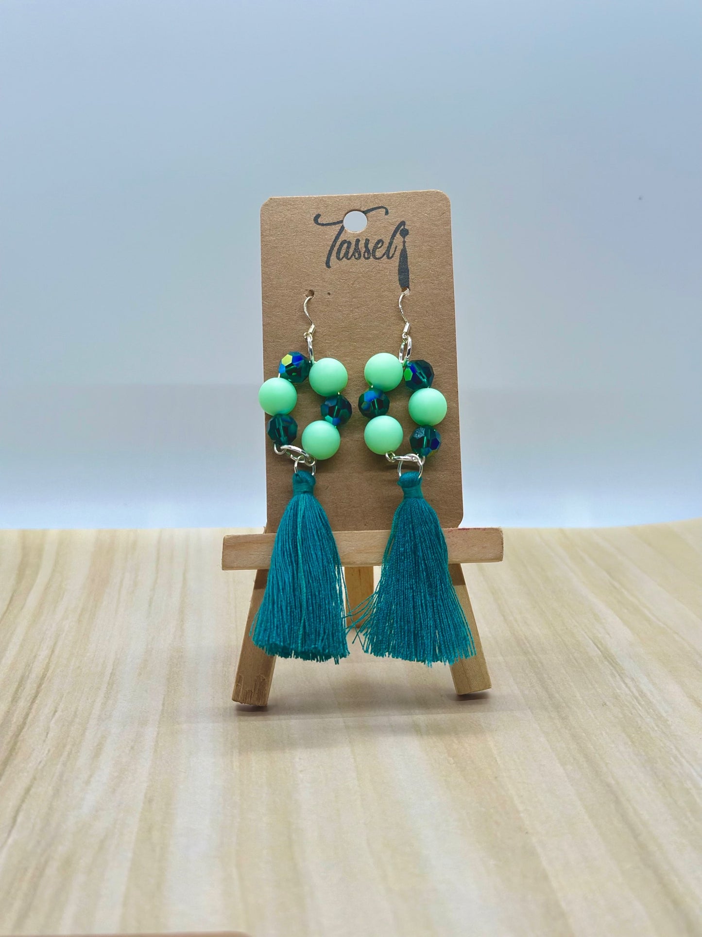 Green circular dangle earrings with bright monochromatic beads and hanging tassel in multiple colors.