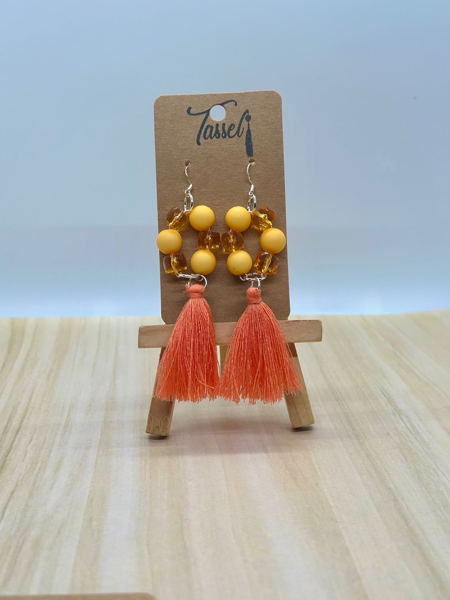 Orange circular dangle earrings with bright monochromatic beads and hanging tassel in multiple colors.