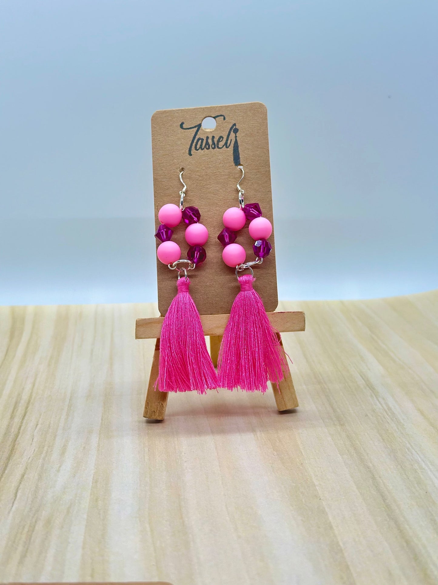 Pink circular dangle earrings with bright monochromatic beads and hanging tassel in multiple colors.