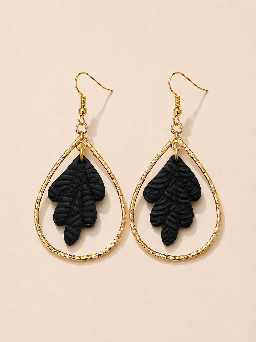 Black leaf-shaped earrings with gold hoop designs on a beige background