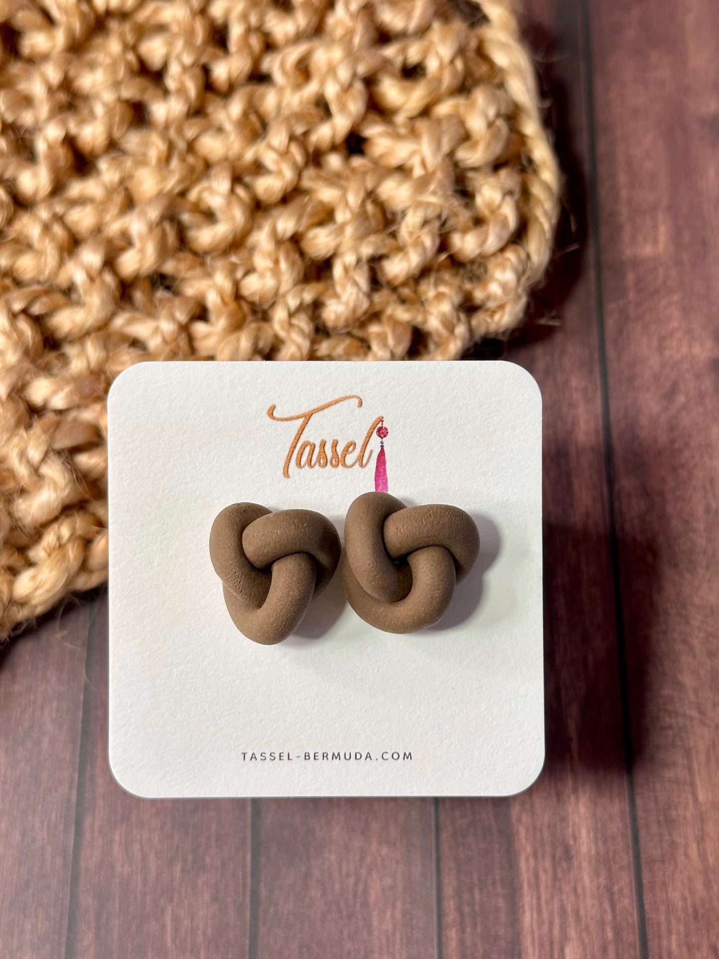 Brown knot-shaped earrings on a Tassel branded card with a textured beige fabric background.