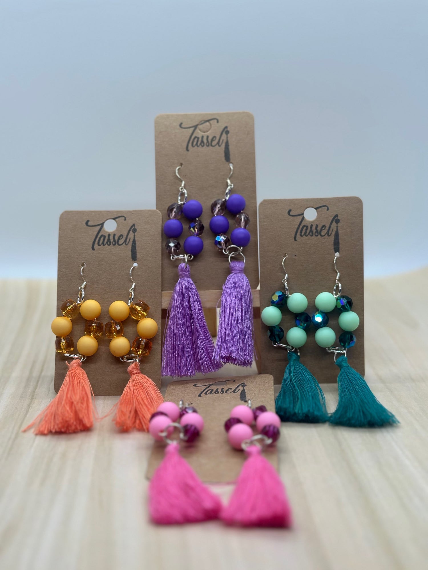 Circular dangle earrings with bright monochromatic beads and hanging tassel in multiple colors.