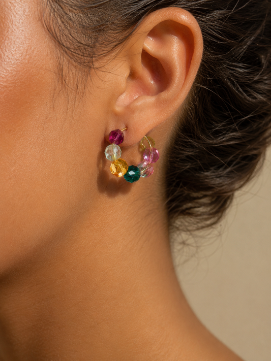 Close-up of an ear wearing colorful gemstone earrings against a neutral background