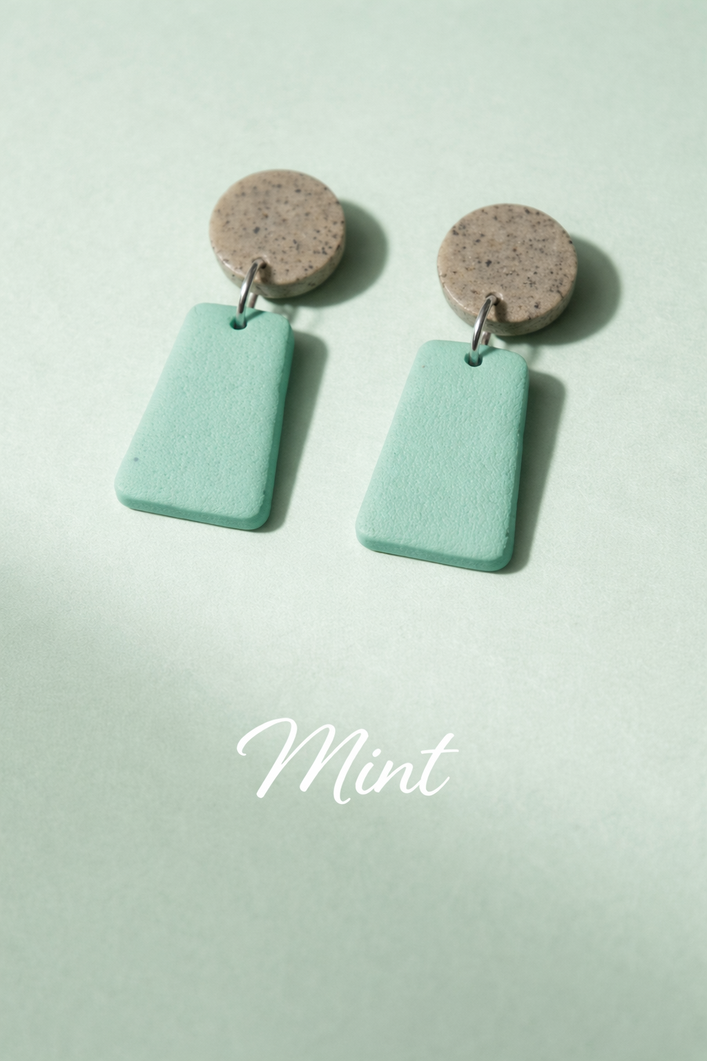 Mint green earrings with brown circular tops on a light green background