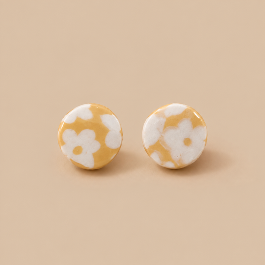 A pair of round stud earrings with a yellow and white floral pattern, displayed on a solid beige background.