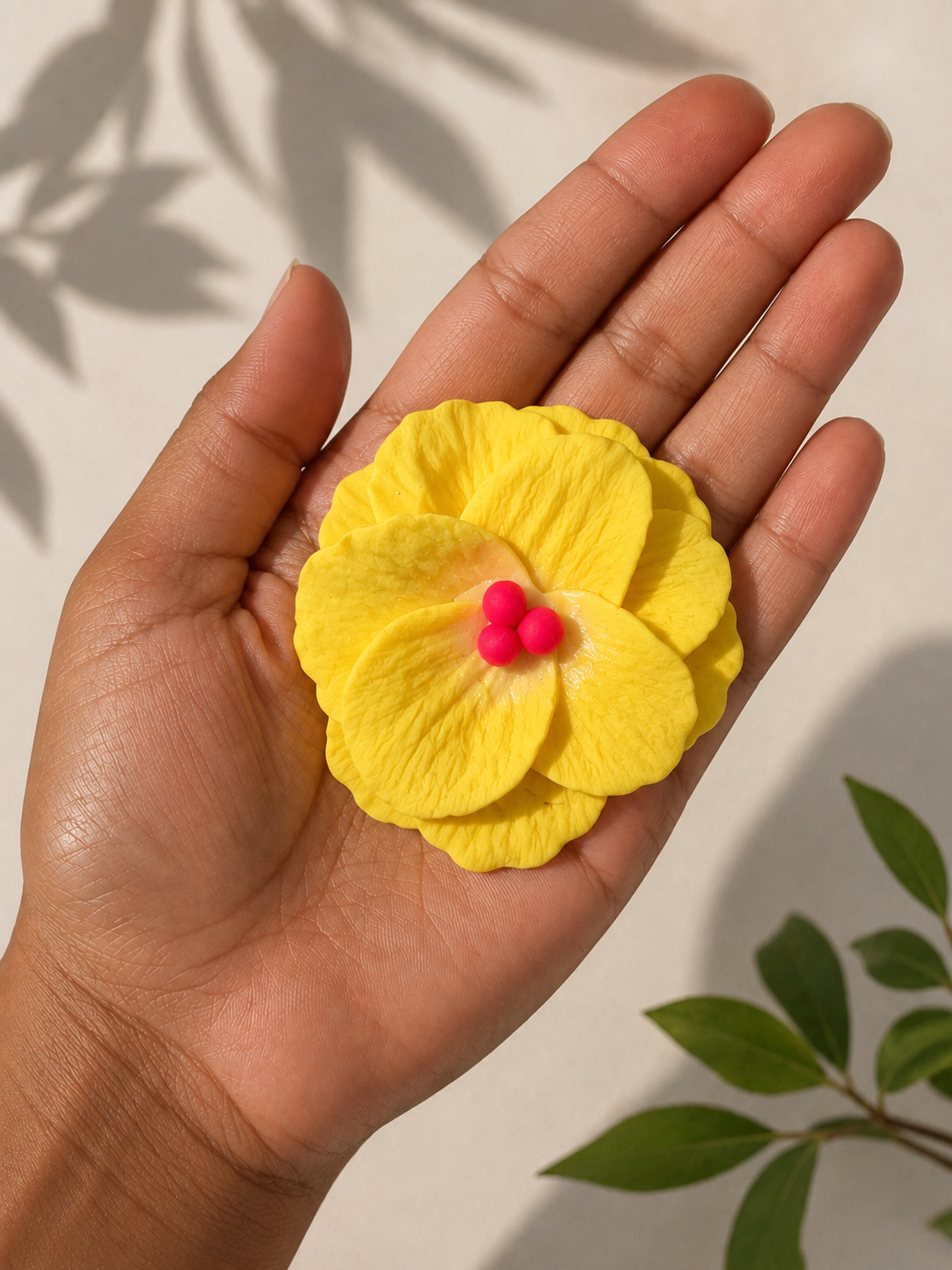 Hand holding a yellow flower with pink center against a neutral background