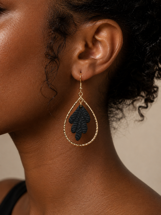 Close-up of a person wearing a gold and black leaf-shaped earring against a neutral background