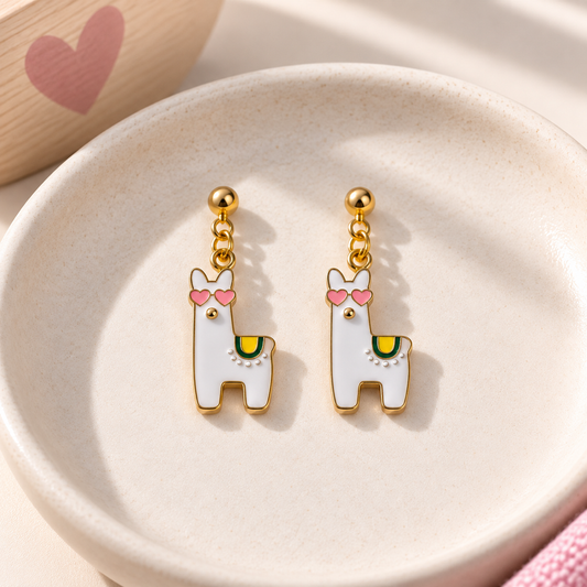 A pair of gold-tone dangle earrings shaped like white llamas with pink heart-shaped sunglasses and a small green accent, displayed on a round beige dish.