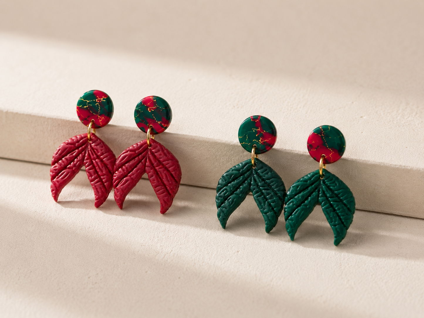 Handmade Jubilee polymer clay dangle earrings with marbled holiday studs and textured botanical leaf charms in red and evergreen.