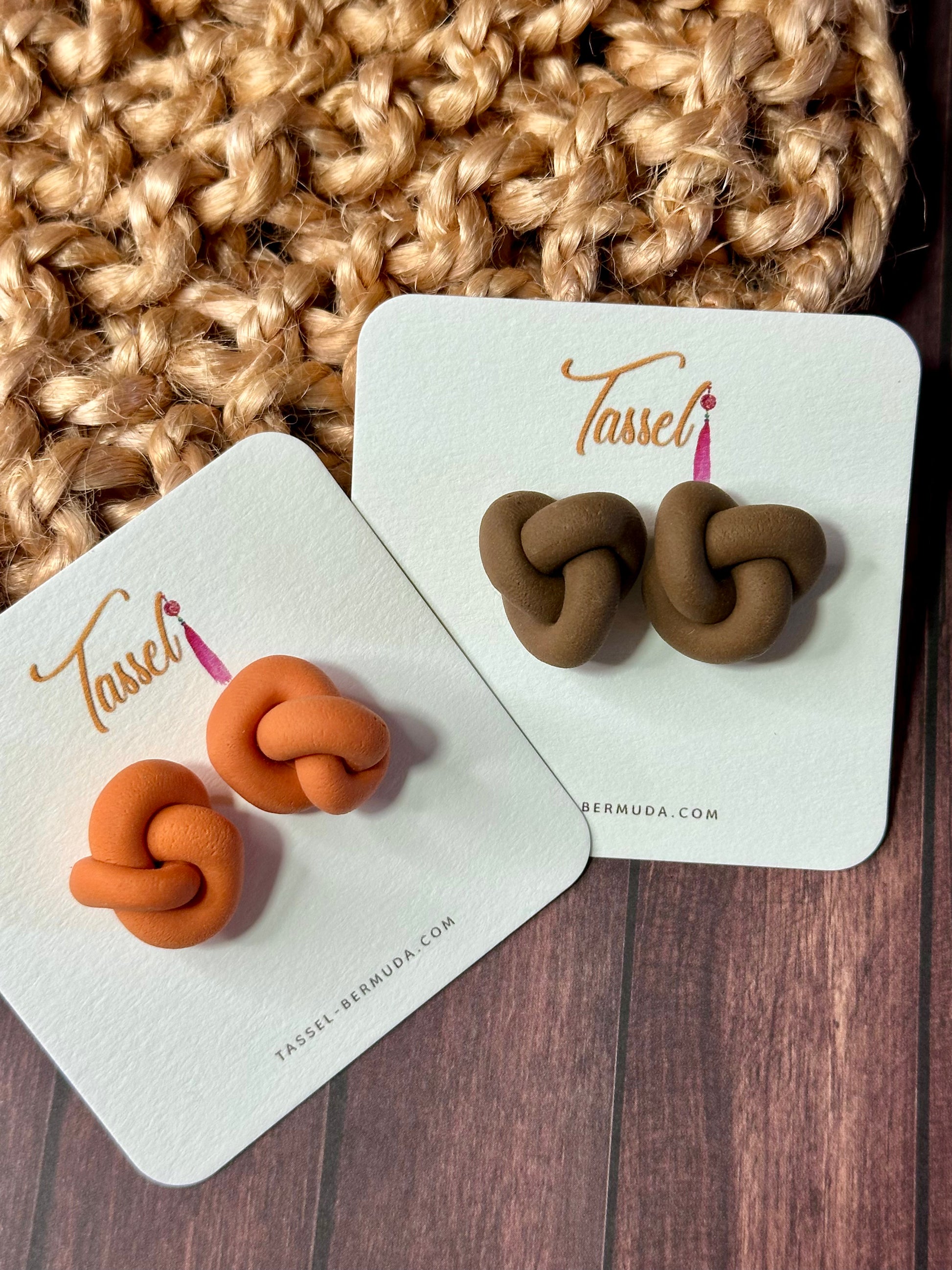 Pair of knot-shaped earrings on Tassel Bermuda branded cards against a textured fabric background.
