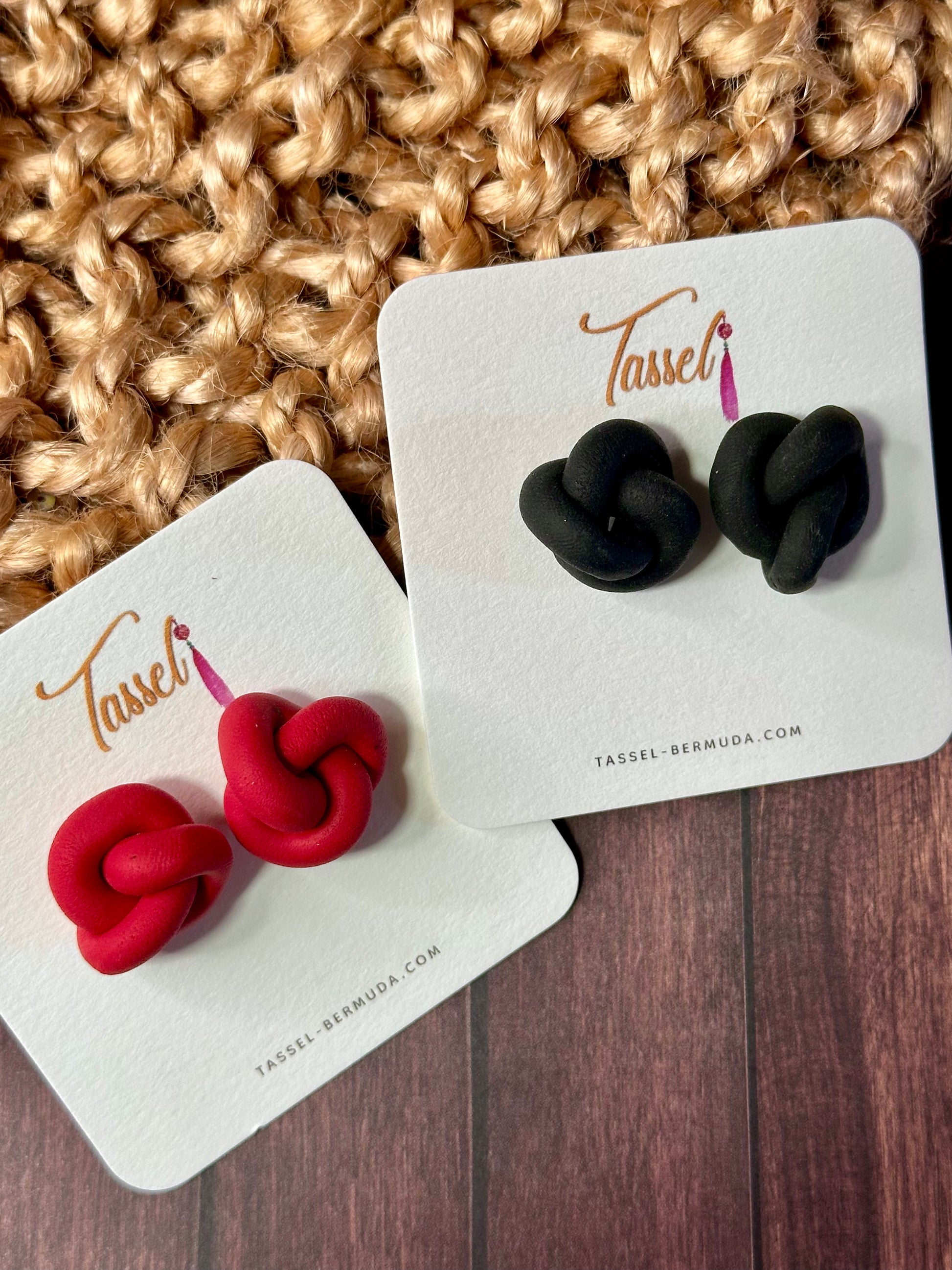 Pair of red and black knotted earrings on Tassel branded cards against a textured fabric background.
