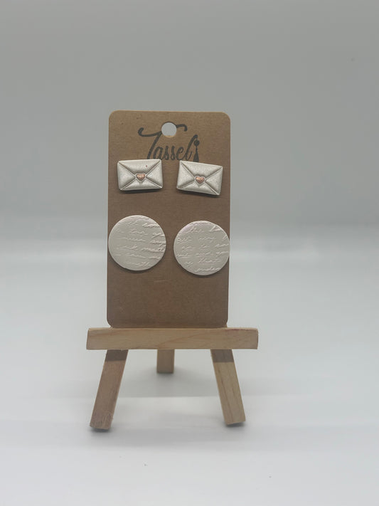 Love Notes polymer clay stud set featuring envelope-shaped earrings and circular handwritten detail studs with shimmering overlay and gold heart accents.