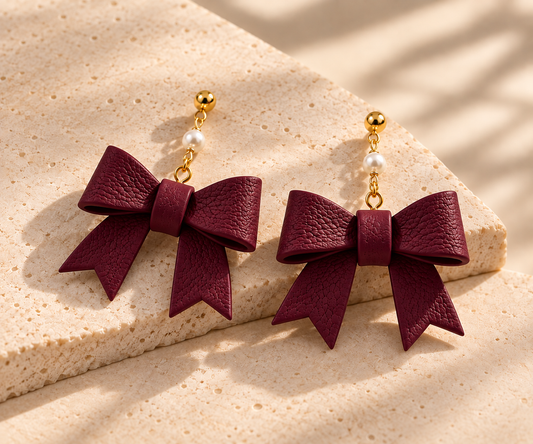 Dangle earrings with a burgundy polymer clay bow and pearl-accented chain. 