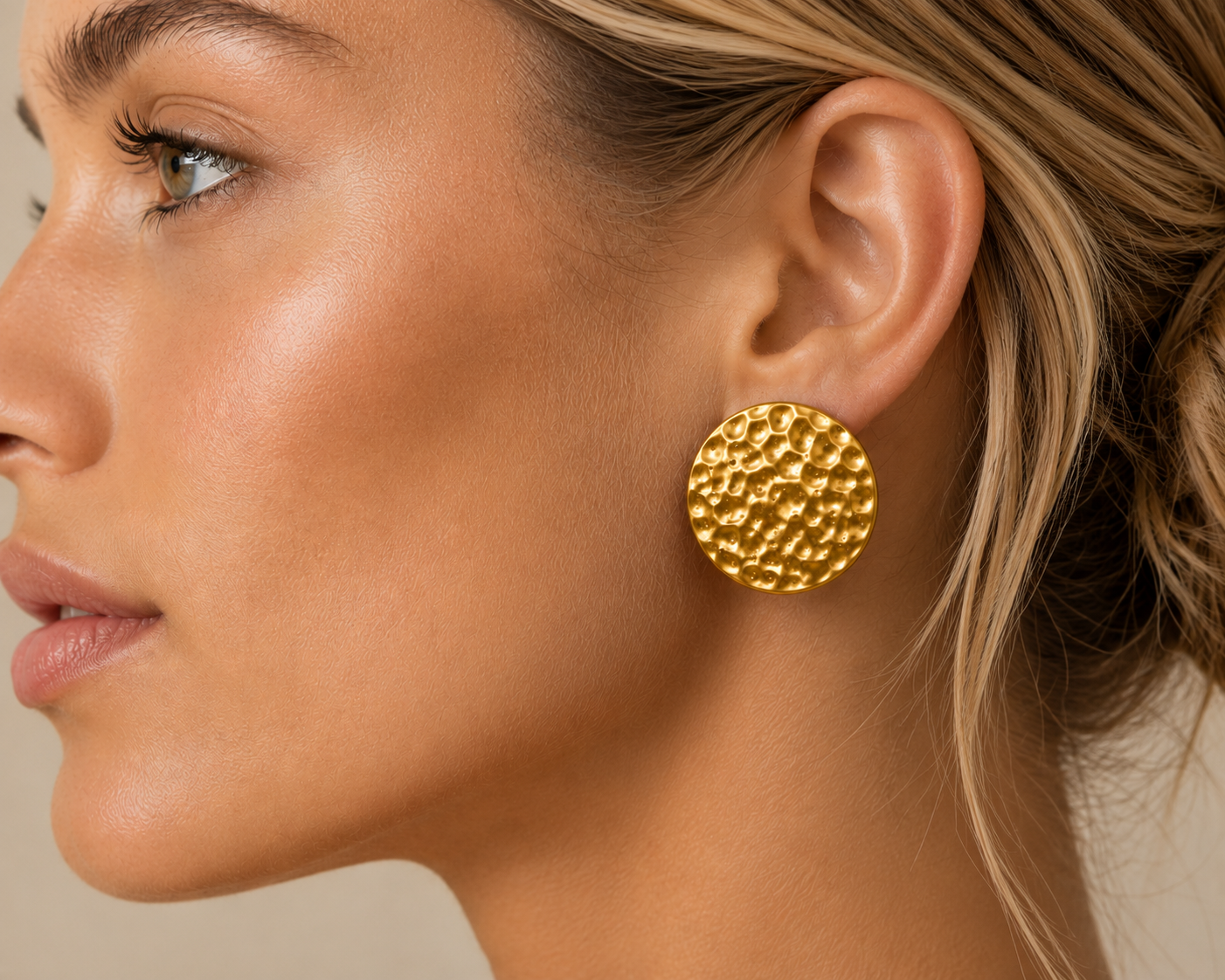 A close-up side profile of a woman wearing a textured gold round stud earring.
