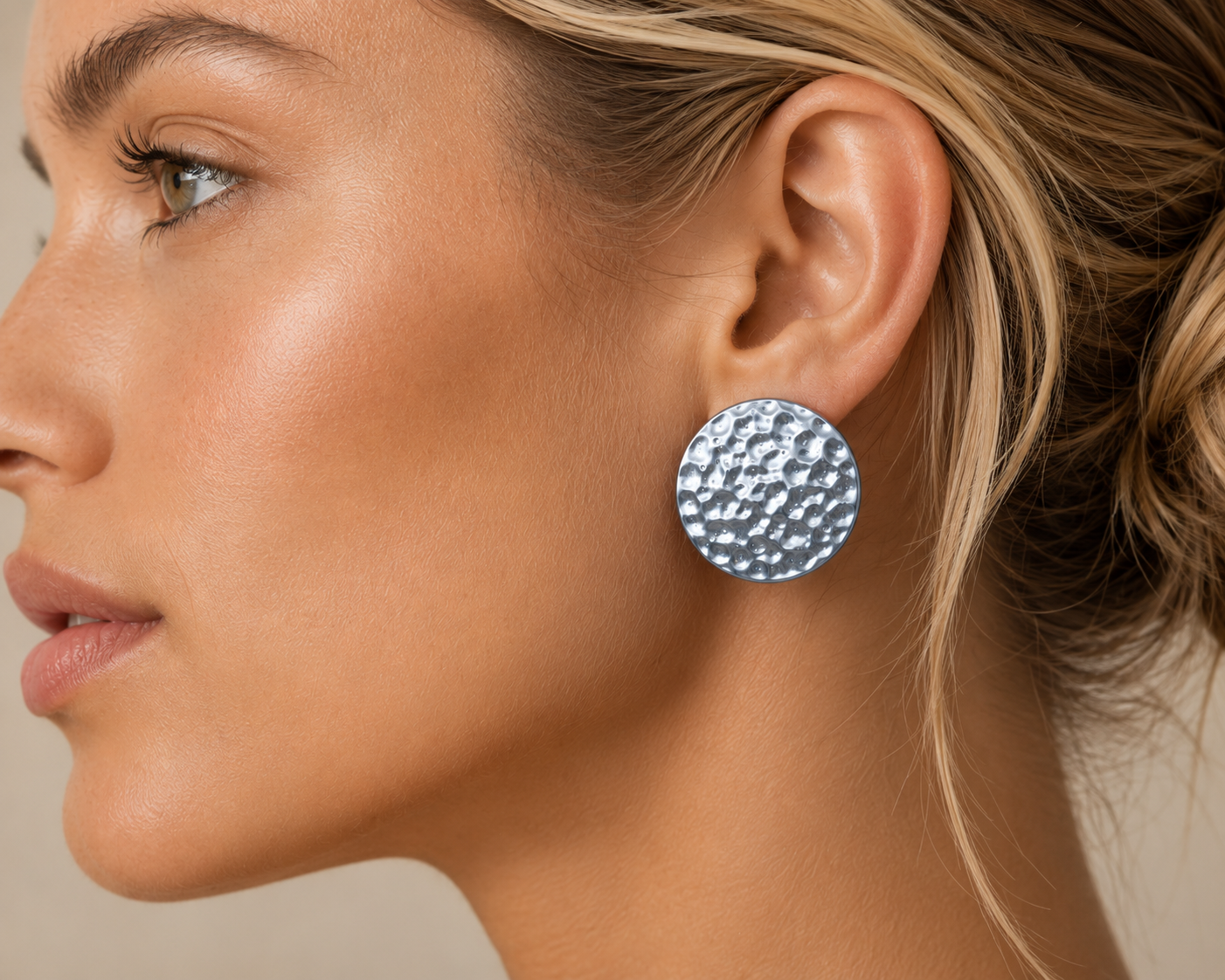 A close-up side profile of a woman wearing a round silver stud earring with a textured, hammered surface.