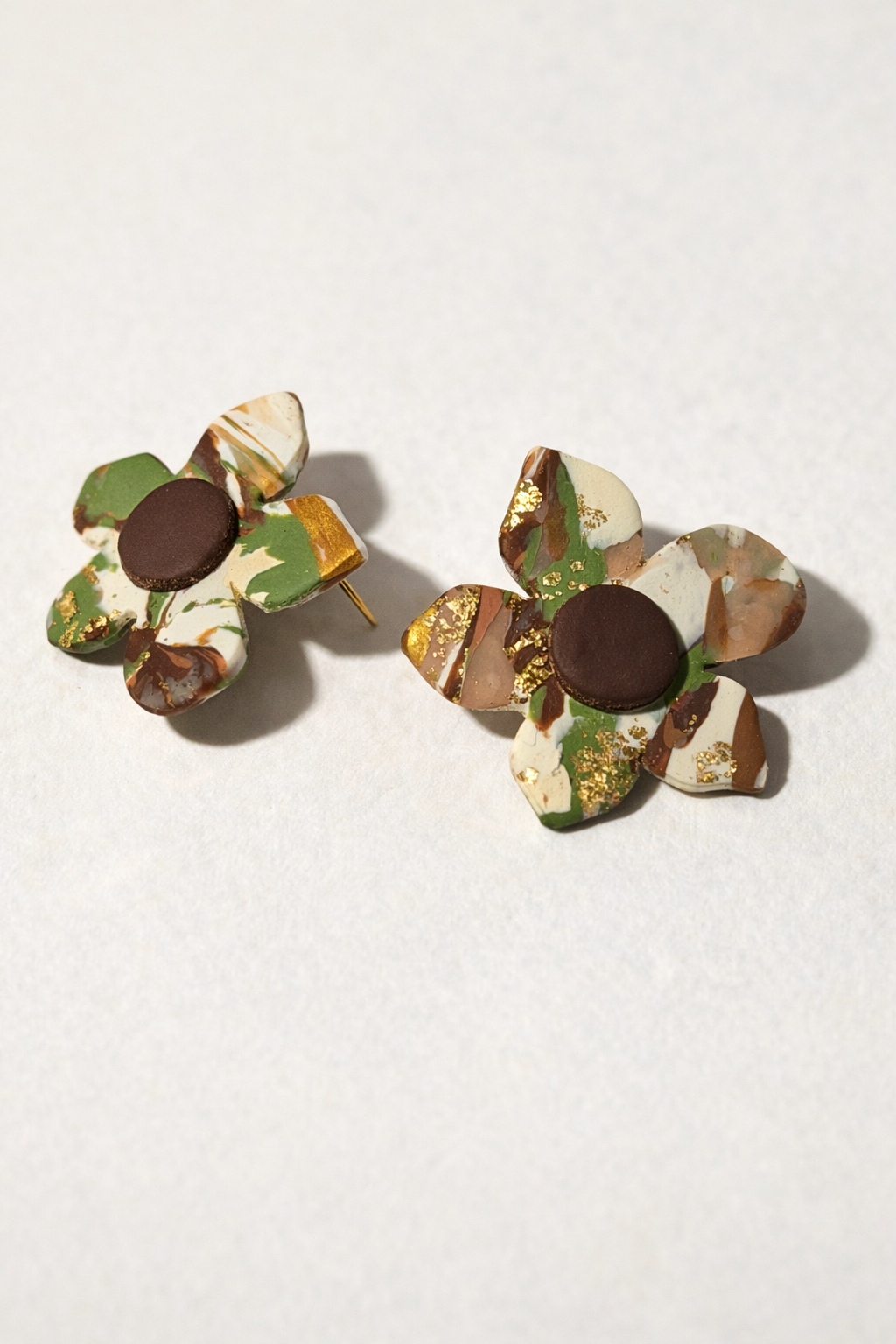 Modern Meadow polymer clay stud earrings with marbled green, brown, and cream tones and gold accents in a floral shape.