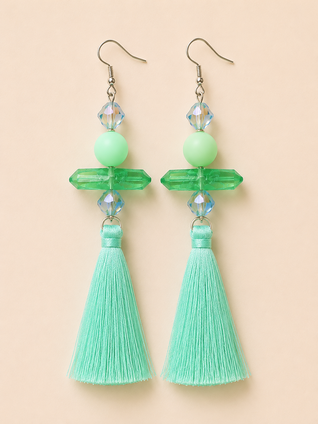 Green tassel earrings with crystal accents on a beige background
