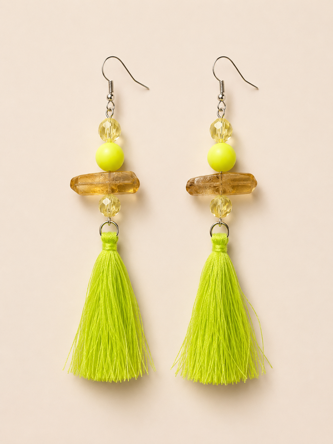 Pair of earrings with yellow beads and green tassels on a beige background
