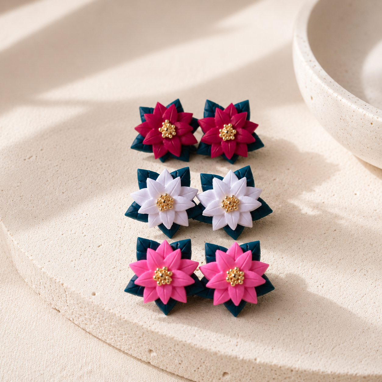 Handcrafted polymer clay poinsettia stud earrings with layered flower petals, gold centers, and evergreen leaves by Tassel Bermuda.