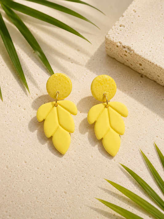 Yellow leaf-shaped earrings on a beige surface with green leaves.