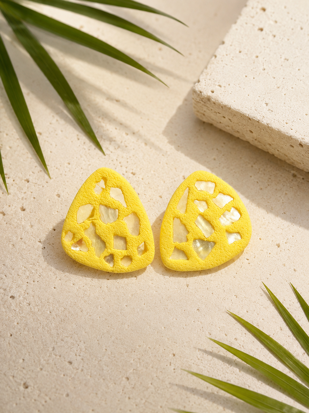 Yellow earrings with shell emballishments on a textured surface with green leaves