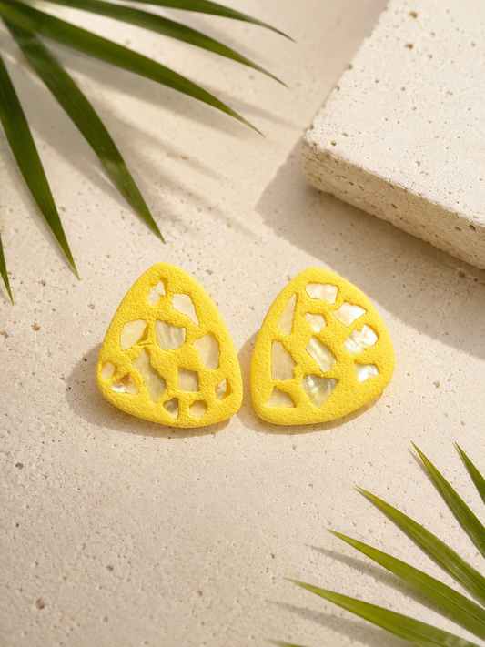 Yellow earrings with shell emballishments on a textured surface with green leaves