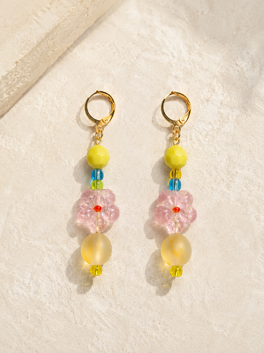 Colorful tropical-inspired dangle earrings with pink floral beads, yellow accents, and gold huggie hoops by Tassel Bermuda.